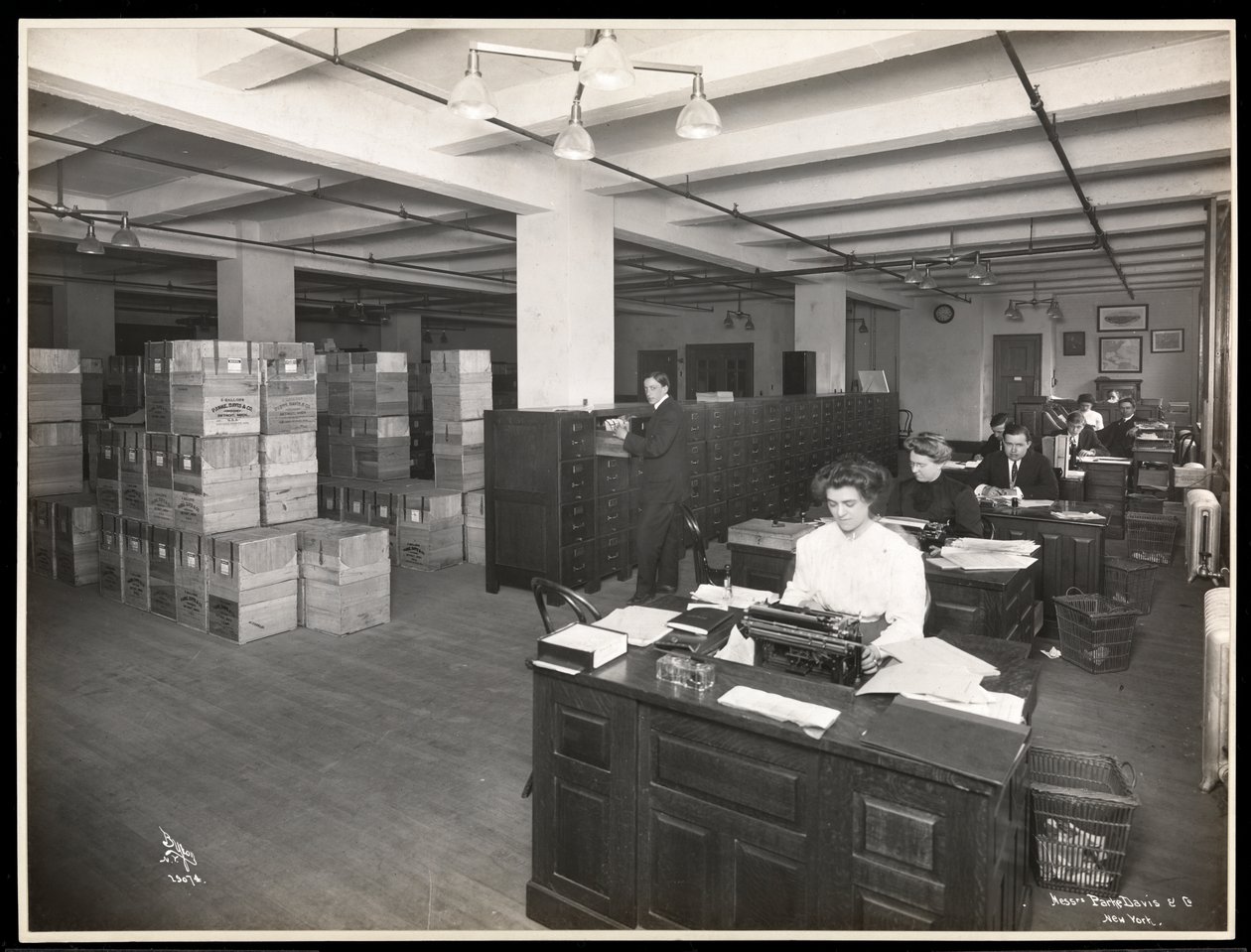 View of men and women at desks in what appears to be a shipping room at Parke, Davis and Co., chemists, Hudson and Vestry Streets, New York, 1910 by Byron Company