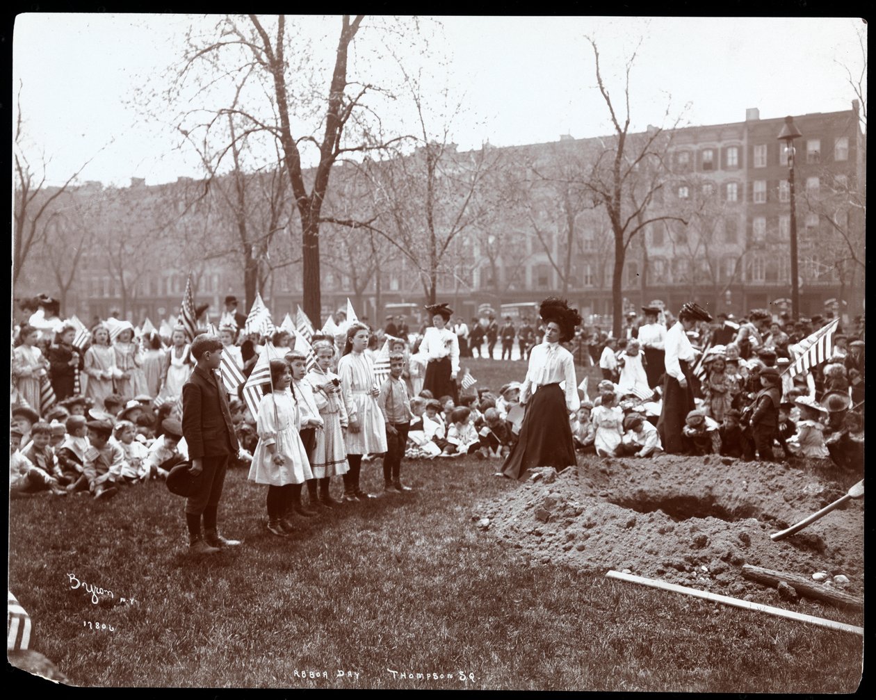 Adults and children holding flags standing around a newly dug hole for a tree planting on Arbor Day at Tompkins Square Park, New York by Byron Company