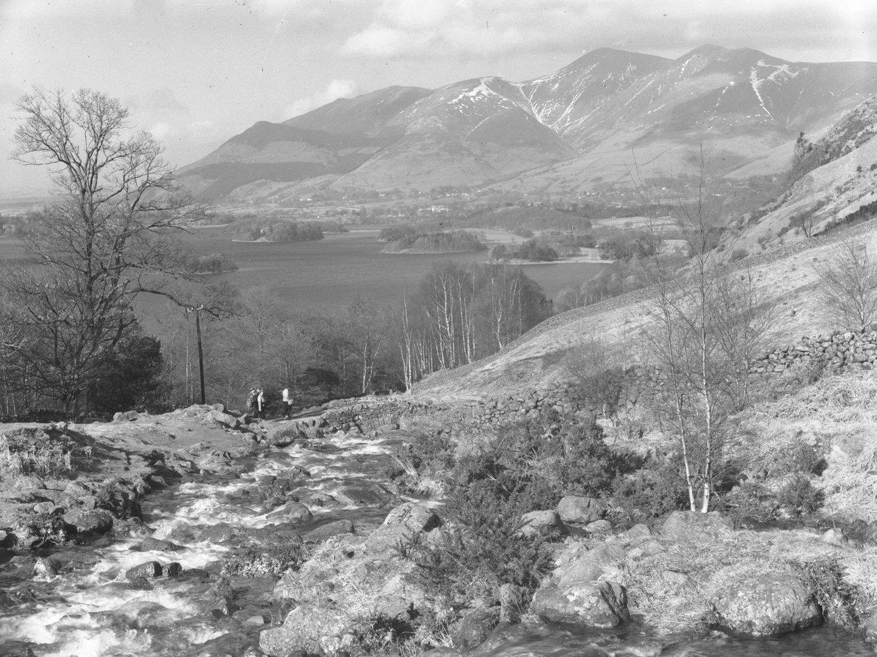 Walkers crossing a dry stone bridge over a stream, hills and lake in background by Joseph Hardman