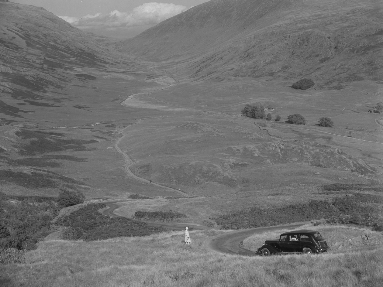 A woman stands overlooking an open valley, with a parked car nearby by Joseph Hardman