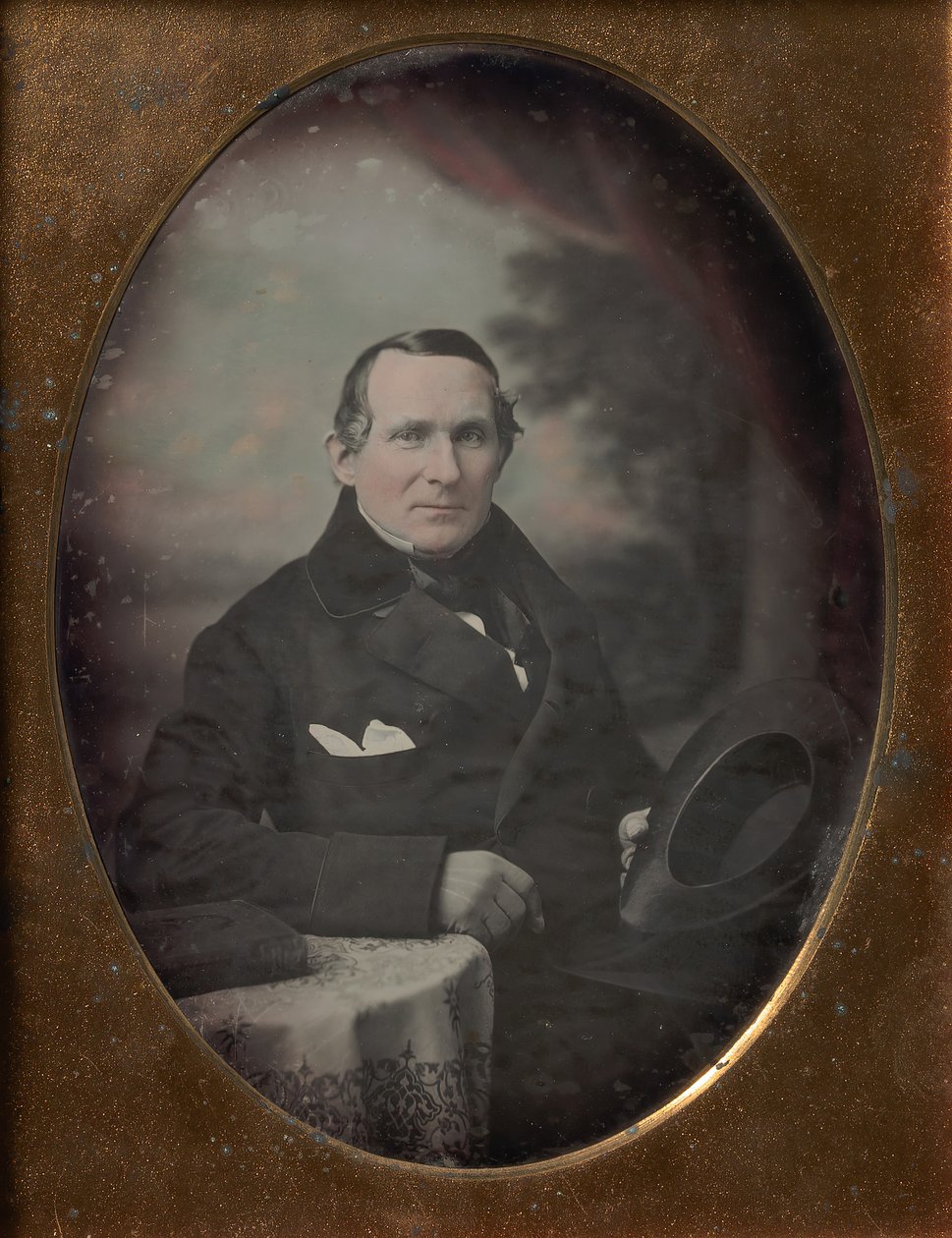 Man Wearing Coat and Gloves, Holding Hat, Seated in Front of Painted Outdoor Backdrop, 1840s by Samuel Broadbent Jr..