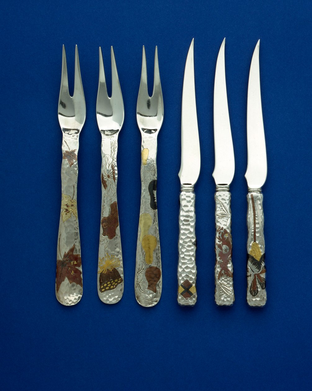 Part of a fine and rare set of 36 dessert knives and forks, the spot hammered handles inlaid with patinated copper and varicolored gold, with engraved details of various floral, animal and geometric designs, c.1880 by Tiffany and Company