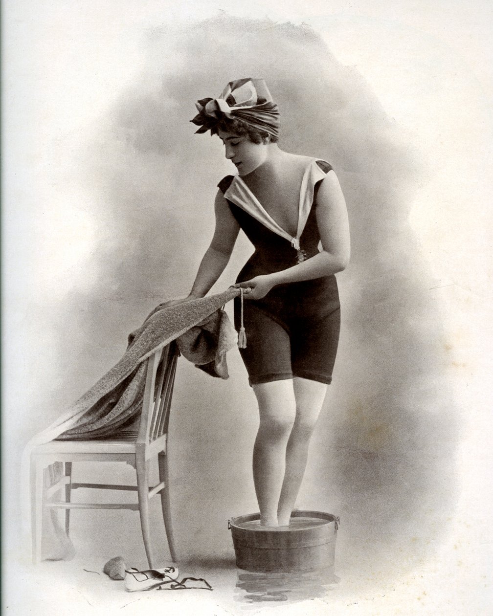 Young woman in a swimsuit taking a foot bath around 1900