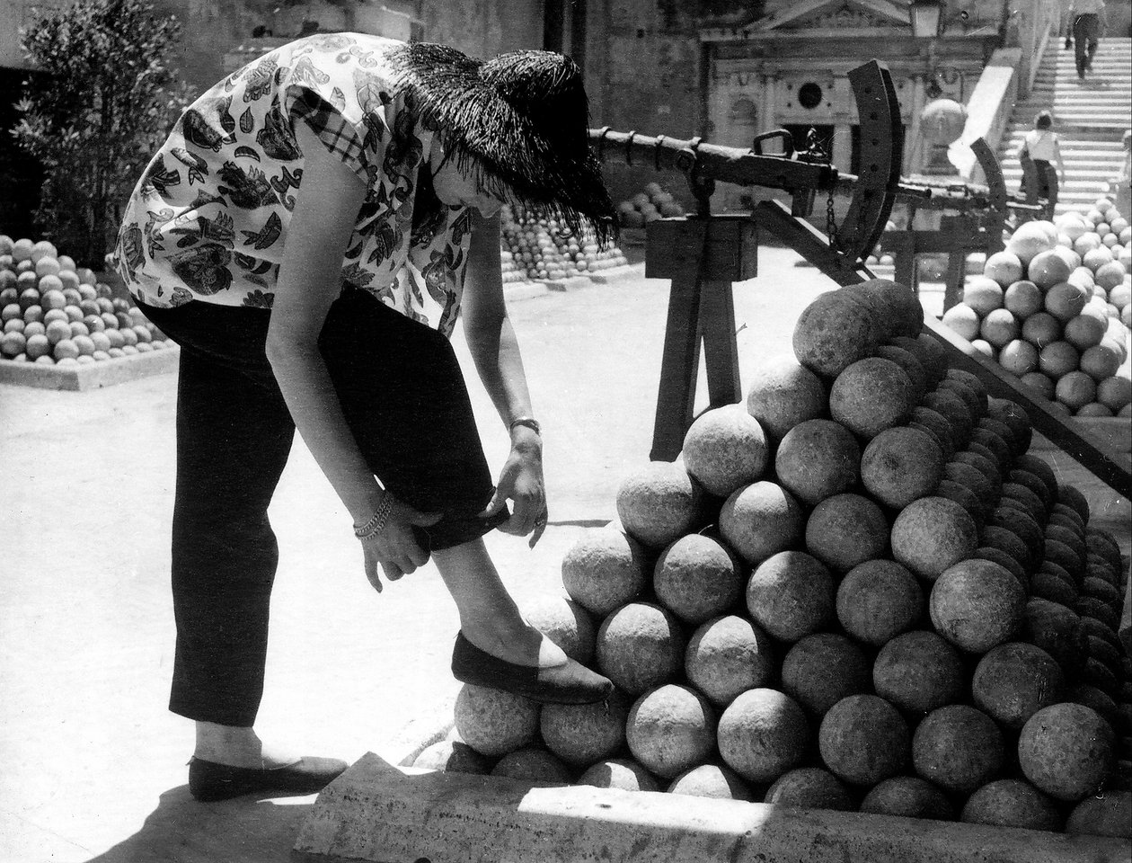 A woman adjusts the cuff of her pants as she rests her foot on a pile of cannonballs inside the grounds of Castel Sant