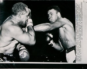 Young Cassius Clay scores with a left against the veteran Archie Moore in the first round of the fight in Los Angeles by American Photographer