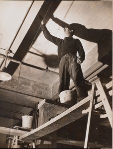Man standing on wooden scaffolding painting a ceiling