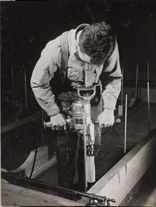 Man uses a handheld machine to work with a piece of wood by Arnold Eagle