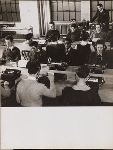 People sit in front of typewriters while wearing headphones by Arnold Eagle