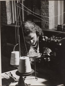 Woman using a sewing machine with two spools of white thread by Arnold Eagle