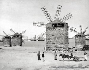 Windmills on the Mediterranean Sea in Alexandria, Egypt. In front, some Egyptians posing with a small cart
