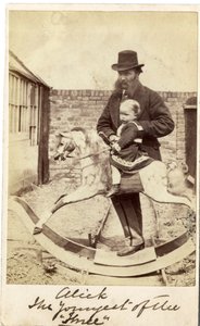 Young girl on a rocking horse in the garden, her father beside by English Photographer