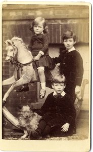 Young girl on rocking horse with one boy standing and one boy seated with dog by English School