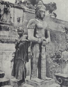 Young Buddhist novice monk beside a statue of the Buddha, French Indochina by Ewing Galloway