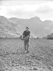 Man sowing seed from swill basket with Langdales behind