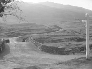 View of the road passing over Hardknott Pass with a sign pointing in the direction of Hardknott