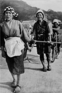 Three generations of women moving a cart with grandmother at the rear, pushing, c. 1900, 1921