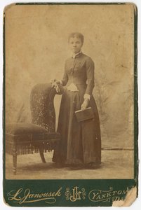 Photograph of a woman standing next to a chair and holding a book by Louis Janousek