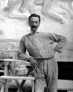 Portrait of the famous sculptor Pietro Canonica in work clothes. The artist is posing in his studio holding a tool of his trade in his right hand