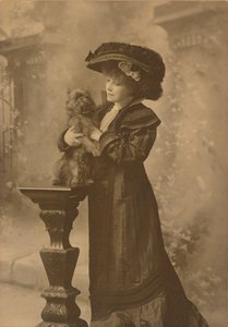 Sarah Bernhardt Standing in a Studio Setting, Holding a Little Black Dog on an Ornate, Carved Wooden Pedestal by Theodore C. Marceau