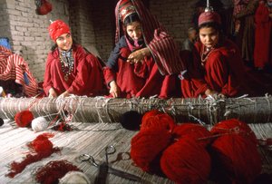 Turkoman tribeswomen weavers trim knots in the warp of a rug on a loom in a village by Thomas J. Abercrombie