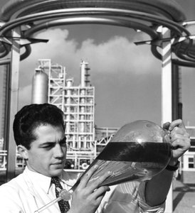 A laboratory worker holds a separating funnel of oil, Dunkirk refinery, France, 1950s