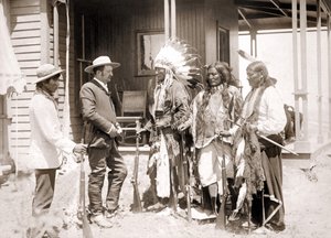 Three Cheyenne dressed in ceremonial costume and wearing guns greet a White accompanied by an interpreter