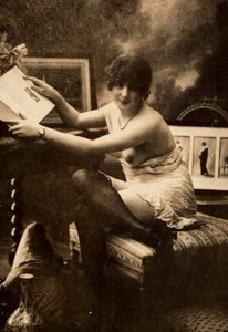 Portrait of a young woman in intimate apparel, seated at a table with a book by Unknown photographer