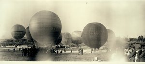 Hot air balloons at a field in South St. Louis ready for launch; one is already in the sky in the distance