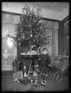 Seymour boy posed with tricycle beside Christmas tree in parlor, Christmas 1912