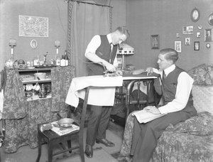 Unidentified Man Demonstrating the Use of an Electric Iron, Watched by Another Man, c.1913-14