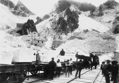 Excavators in front of a railroad convoy loaded with blocks of marble at Ravaccione, in the Apuan Alps by A. Corsini