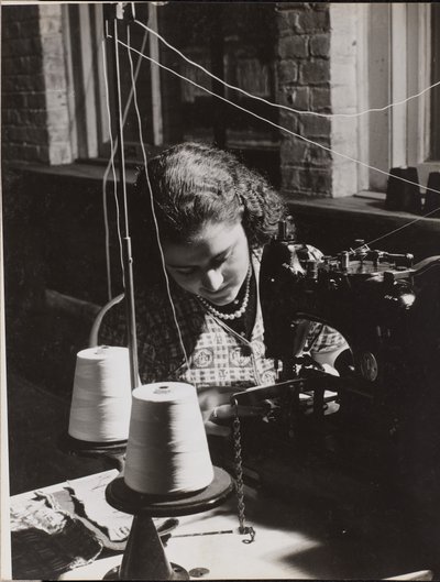 Woman using a sewing machine with two spools of white thread by Arnold Eagle