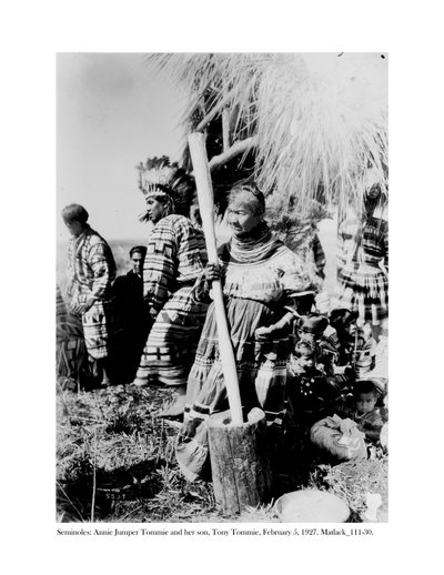 Annie Jumper Tommie Using a Mortar and Pestle to Make Cornmeal, and Her Son, Tony Tommie, Wearing an Eagle Feather Bonnet by Claude C. Matlack