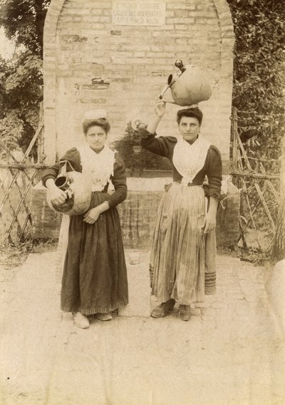 Two young women wearing traditional clothes and carrying terracotta jars near well, Marche, Italy, circa 1910 by Italian Photographer
