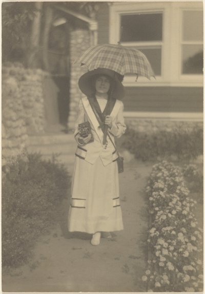 Woman Standing in Front Yard with Camera and Plaid Umbrella by Louis Fleckenstein