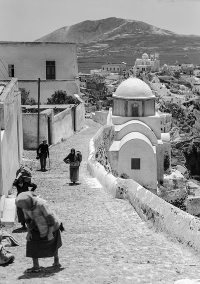 Greek village people walk up cobblestone road in a Greek village with whitewash buildings by Maynard Owen Williams