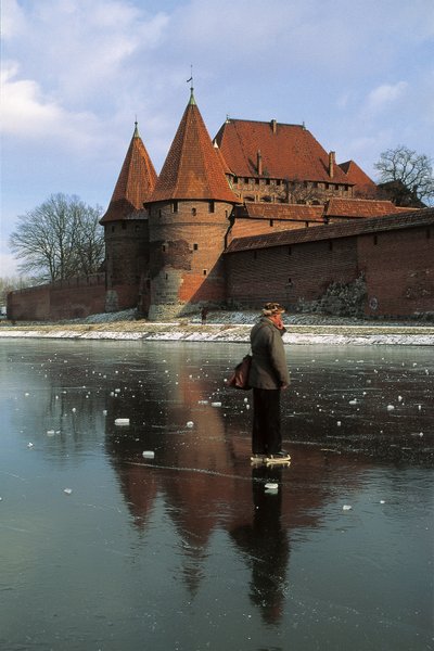 Side profile of a man standing on a frozen river in front of a castle, Nogat River, Malbork Castle, Malbork, Pomorskie Province, Poland by Benjamin Baud