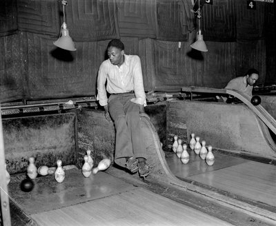 African-American man attending ten pins at bowling alley, to manually reset the pins by Volkmar Wentzel