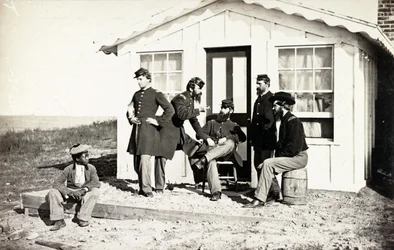 Five Civil War soldiers gathered on dirt porch outside home, African American youth seated near them