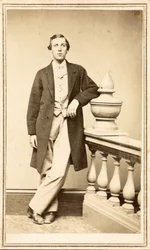 Unidentified man in top coat leaning against pillar, c.1860-75