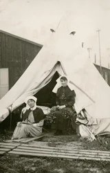 Sister Eleanor Wibmer Jeffries and Sister Nellie Constance Morrice outside their tent at No 3 Australian General Hospital with flowers picked from the bank of the Somme, c. June 1917