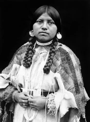Cayuse woman, half-length portrait, standing, facing front, braids, shell disk earrings, shell bead choker and shell beads around neck, beaded buckskin dress with beaded belt c. 1910, photo Edward S. Curtis