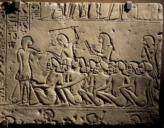 A group of Negroid prisoners surrounded by guards armed with clubs while a scribe draws up a report, relief from the tomb of Horemheb at Saqqara