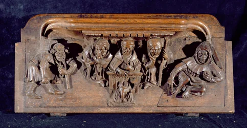 A misericord depicting an academic seated at a panel desk delivering an admonition to a kneeling penitent, New College Chapel, Oxford, late 14th century