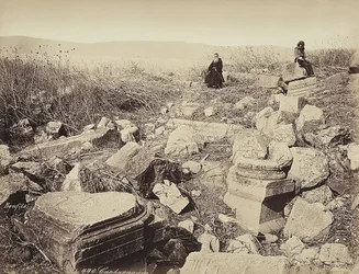 A monk and a man with a gun pose, sitting on some ruins, near Capharnaum