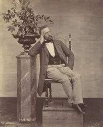 Mathias Höusermann seated with elbow on pedestal holding a vase of flowers