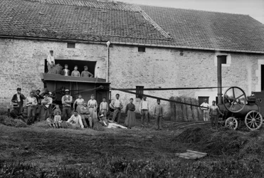 Agricultural workers and the press tied hay boots on a farm near Bourmont in Haute-Marne, around 1890. Photography. Ducos Collection.