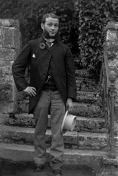 Portrait of a young man from Bourmont in Haute-Marne, wearing the cockade of conscripts at the buttonhole, posing in the garden of the Abbey of Septfontaines. Photography, late 19th century. Ducos Collection.