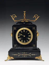 A Mantle Clock of Black Composition Stone, with Incised Decoration, with Legs, Finials and Fittings in Gilt Brass, by Jausions of Pau, France, c.1876-78