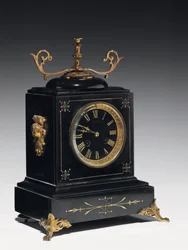 A mantle clock of black composition stone, with incised decoration, with legs, finials and fittings in gilt brass, by Jausions of Pau, France, c.1876-78